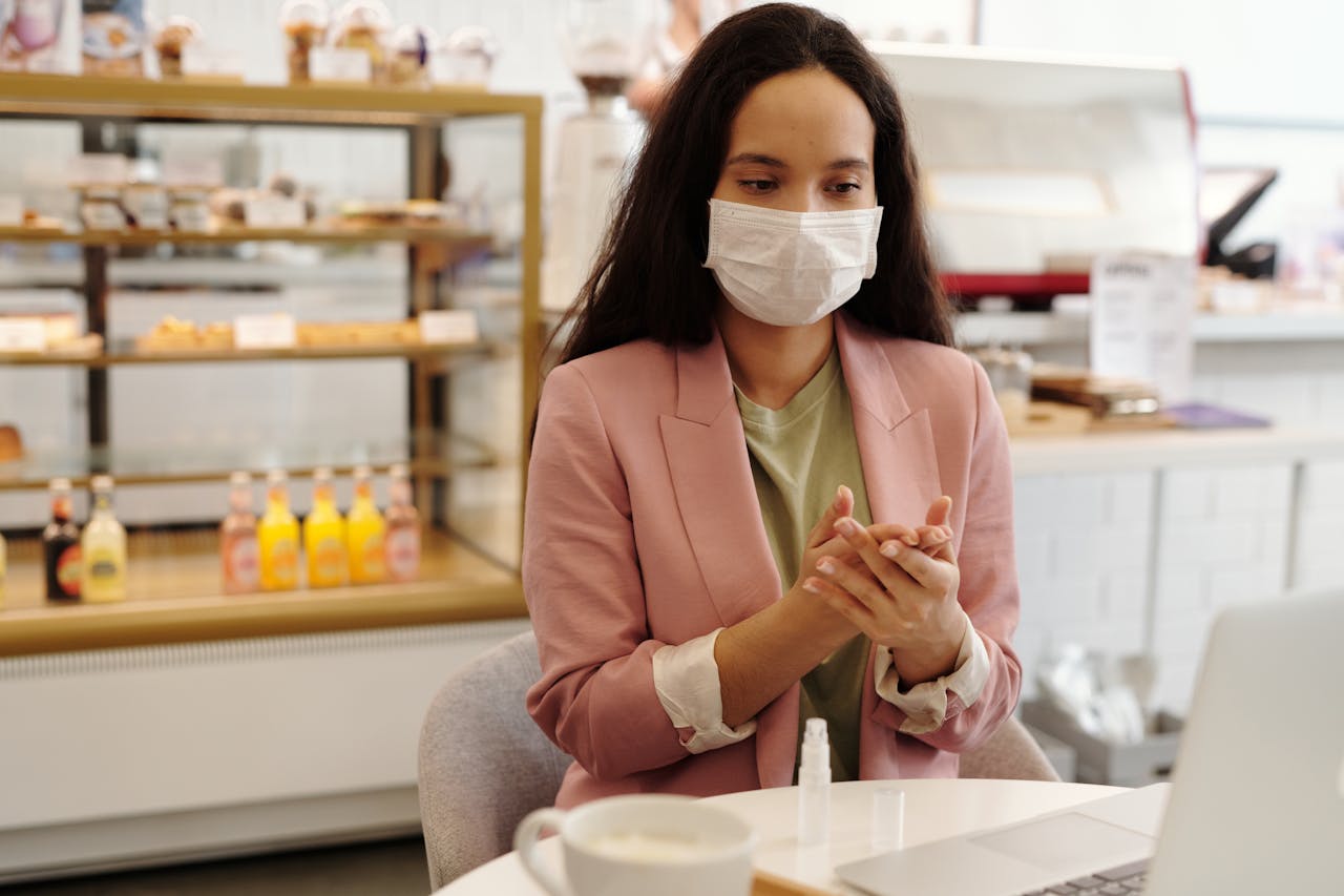 Woman in a cafe sanitizing hands with mask on, practicing hygiene and safety measures.